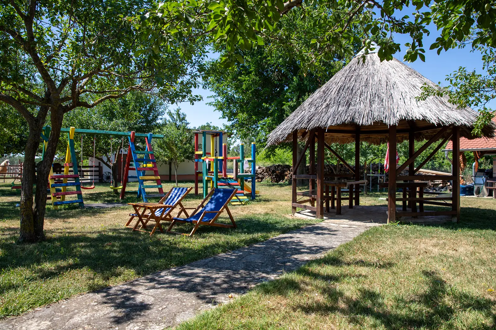 Sjenica s trščanim krovom, ležaljke i dječje igralište u dvorištu